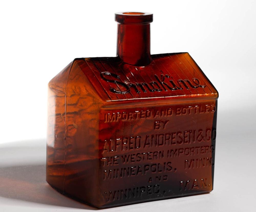 Amber glass figural whiskey bottle with a red-brown hinged lid-style top and embossed label text on the front.
