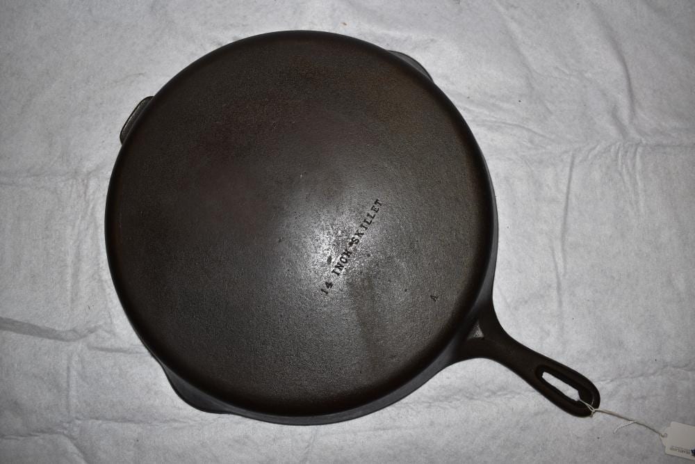 Round black cast iron skillet with a long handle, shown from the underside on a light gray fabric background.