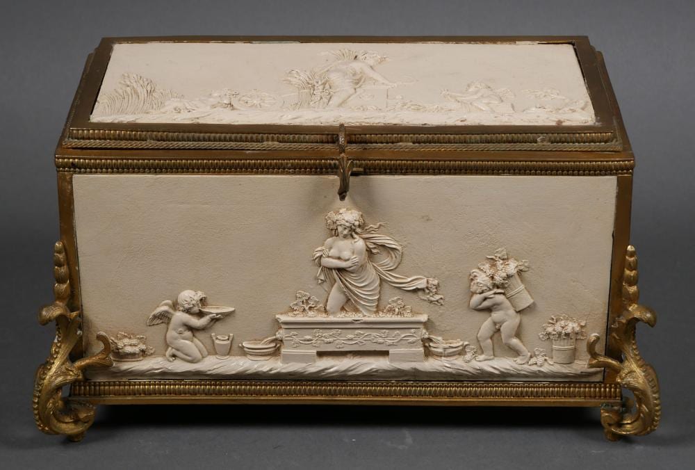 Open rectangular jewelry casket with ornate gold-toned metal mounts and a relief scene of three cherub figures on the front panel.
