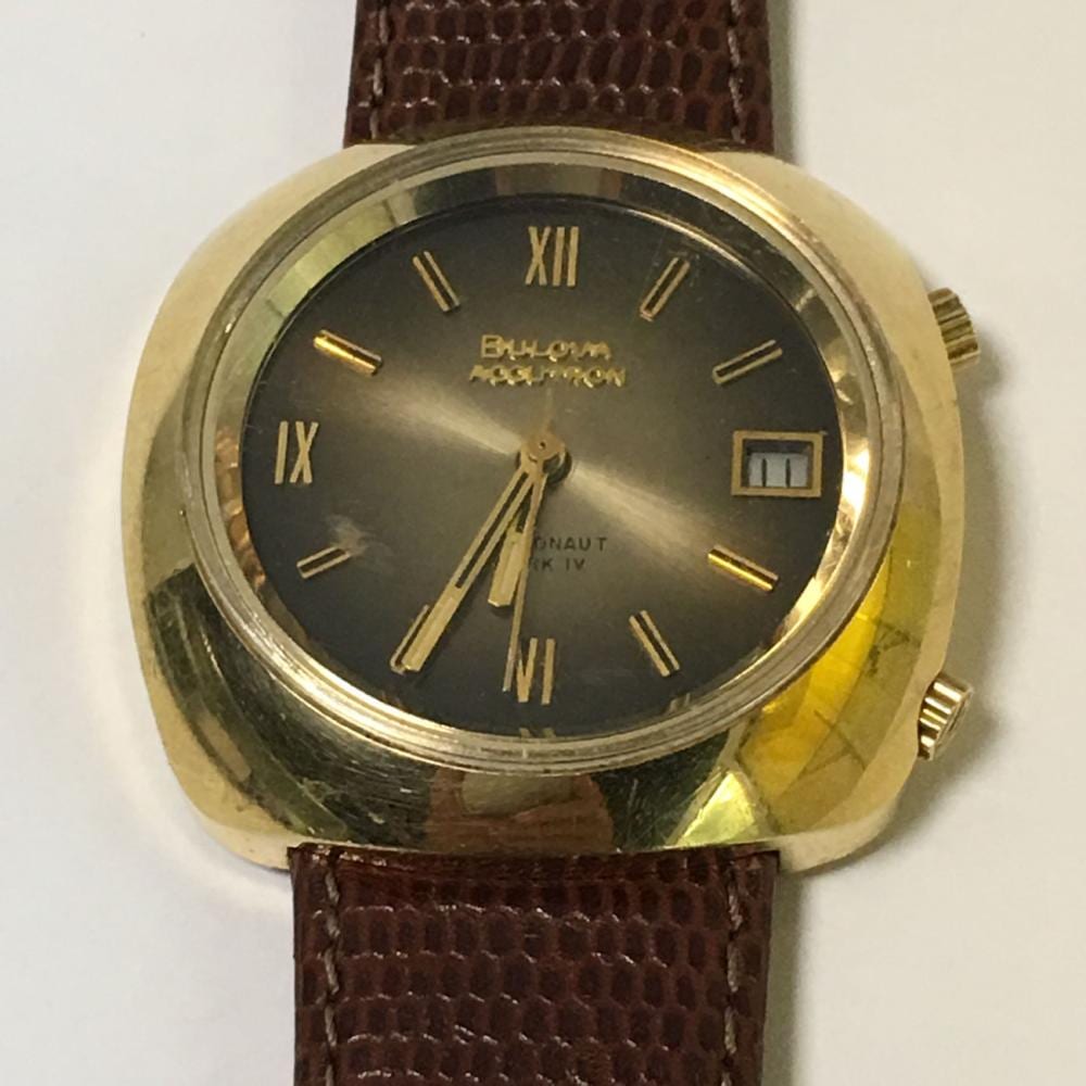 Gold-tone wristwatch with a dark dial, Roman numeral hour markers, and a brown leather strap.