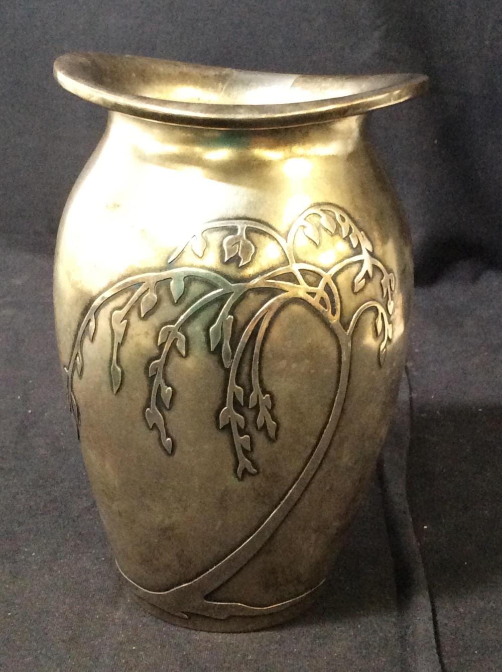 Close-up of a silver-colored art nouveau vase with flared rim and engraved vine and floral decoration on the sides.
