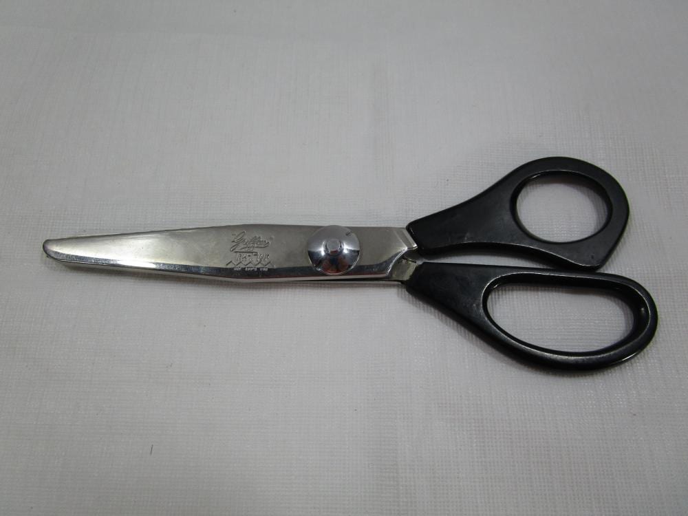 Black-handled metal scissors with two finger loops and a pointed blade, shown on a light fabric background.