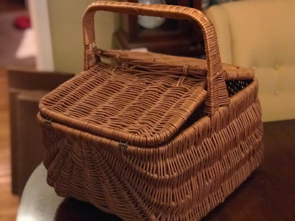Wicker picnic basket with arched handle and woven lid, shown close-up on a table.