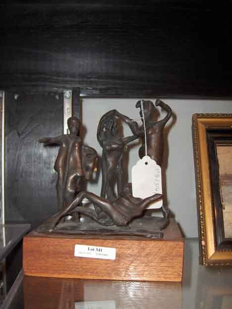 Bronze sculpture group with three figures on a base, set in a display case against a dark background.