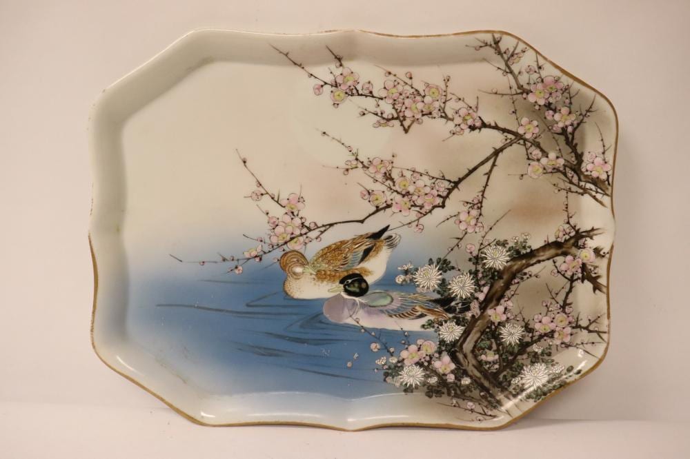 Glazed decorative Japanese-style ceramic plate with a bird perched on a flowering tree over a blue water scene.