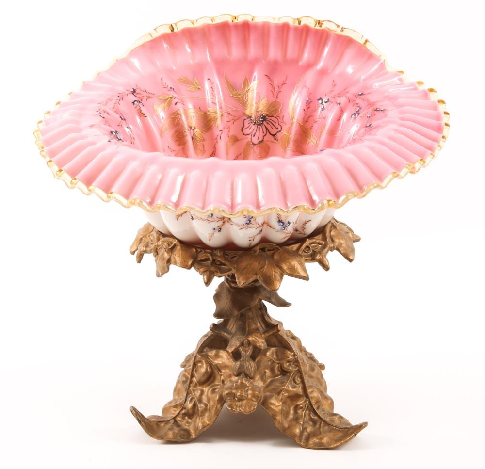 Pink milk glass bowl with a fluted rim and painted floral decoration, mounted on an ornate gold-colored cherub-style pedestal.
