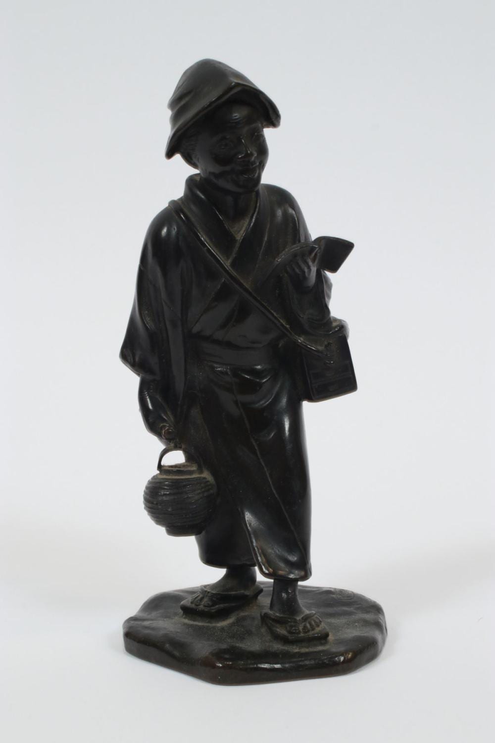 Small dark bronze figurine of a standing man in a traditional robe and hat holding an object at his side.