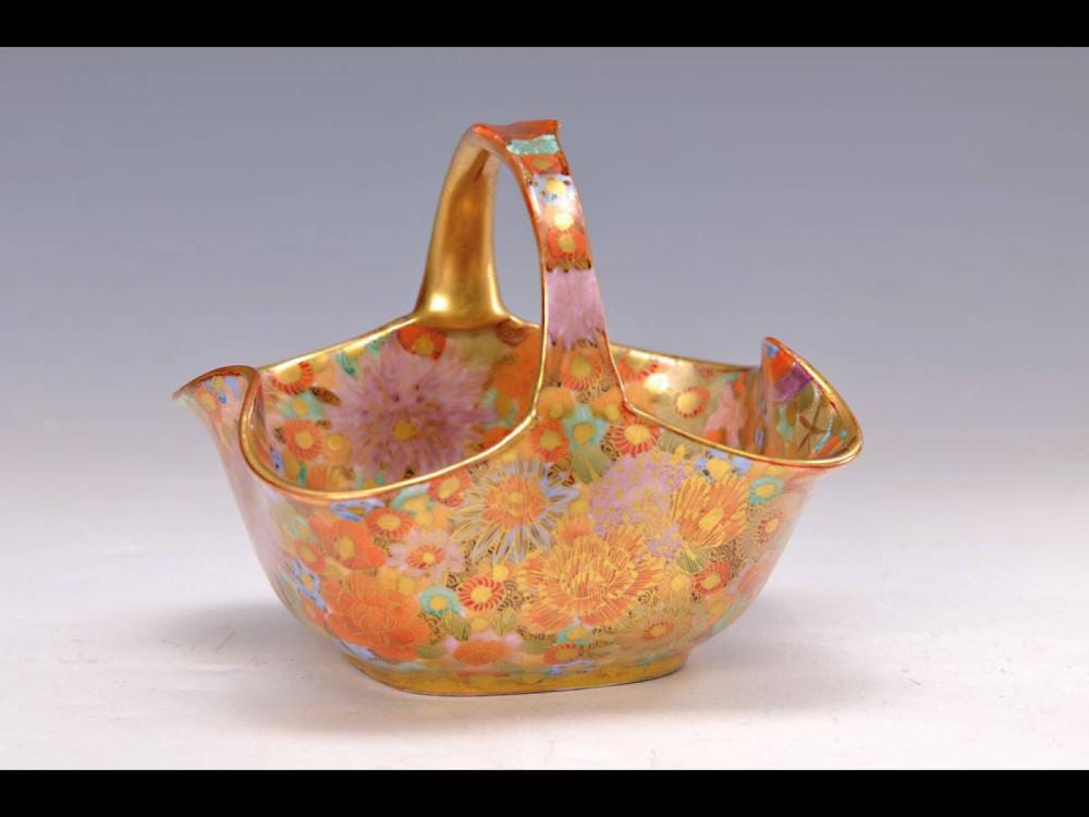 Decorative handled bowl with gold rim and colorful floral pattern, shot against a light gray background.