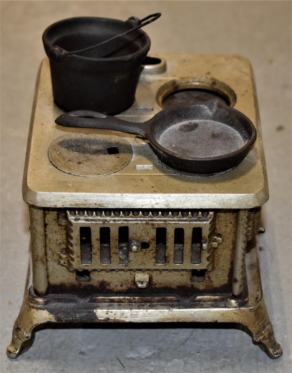 Small cast iron toy stove with two black round pans, a front grill with vertical openings, and a metal handle on top.