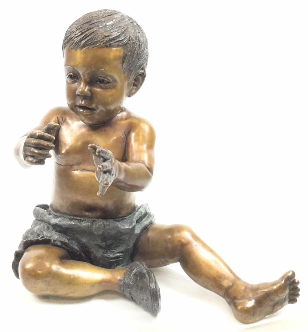 Bronze-style toddler sculpture seated on its legs, with a hand raised holding a small animal figure.