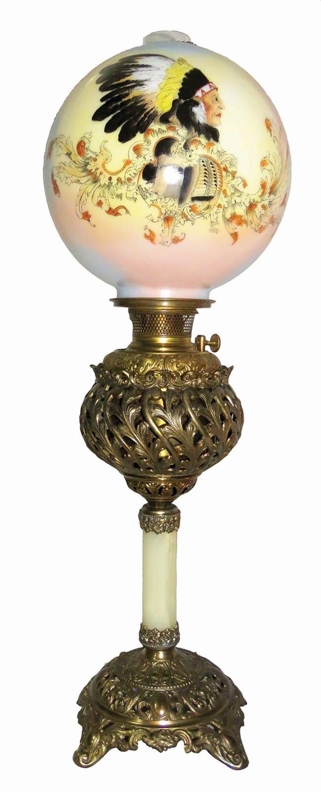 Antique oil lamp with a decorative spherical glass shade painted with a portrait and ornate motifs above a gold-toned base.