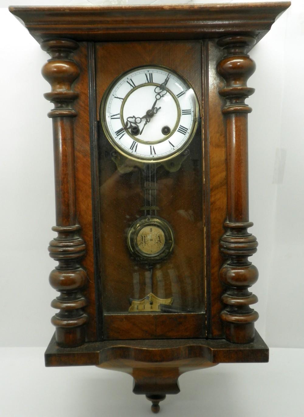 Antique wall clock with a round brass clock face and Roman numerals inside a dark wooden case, shown front view.