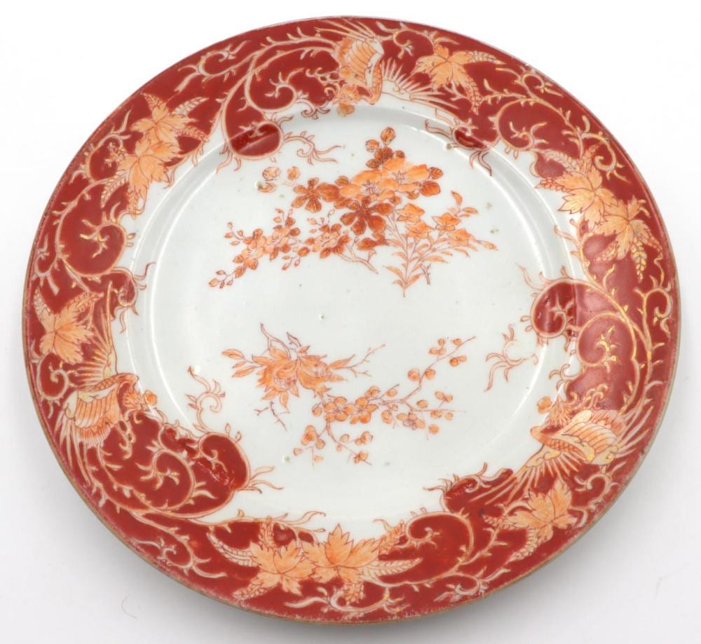Red ceramic plate with gold scrollwork borders and orange floral painted designs in the center.