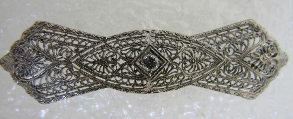 Antique-style gold filigree brooch in a decorative oval shape with an ornate center diamond-shaped stone setting.