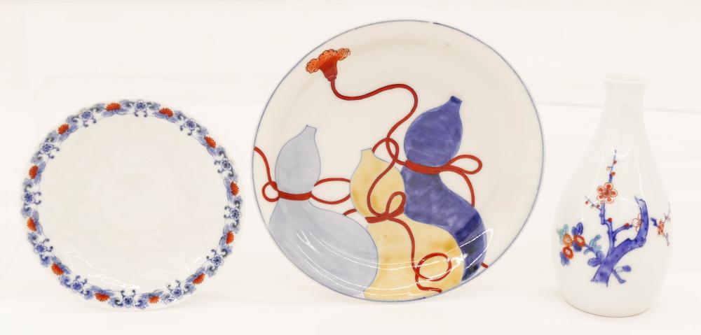Three-piece ceramic set on a white background: two round plates with blue and orange motifs and a white vase with blue floral decoration.