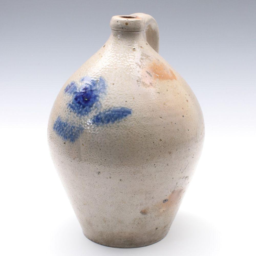 Stoneware jug with an ovoid body and short neck, covered in white glaze with blue floral-like decoration and small speckling.