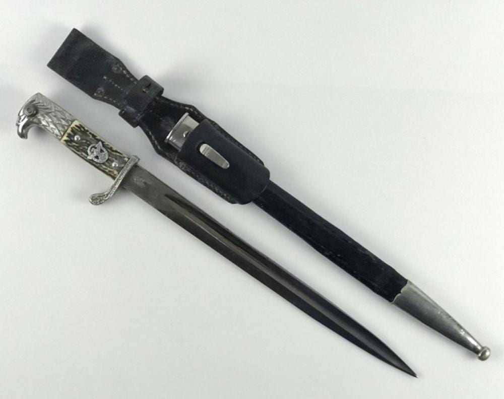 German-style bayonet with a steel blade, ornate silver hilt, and black leather scabbard laid on a white background.