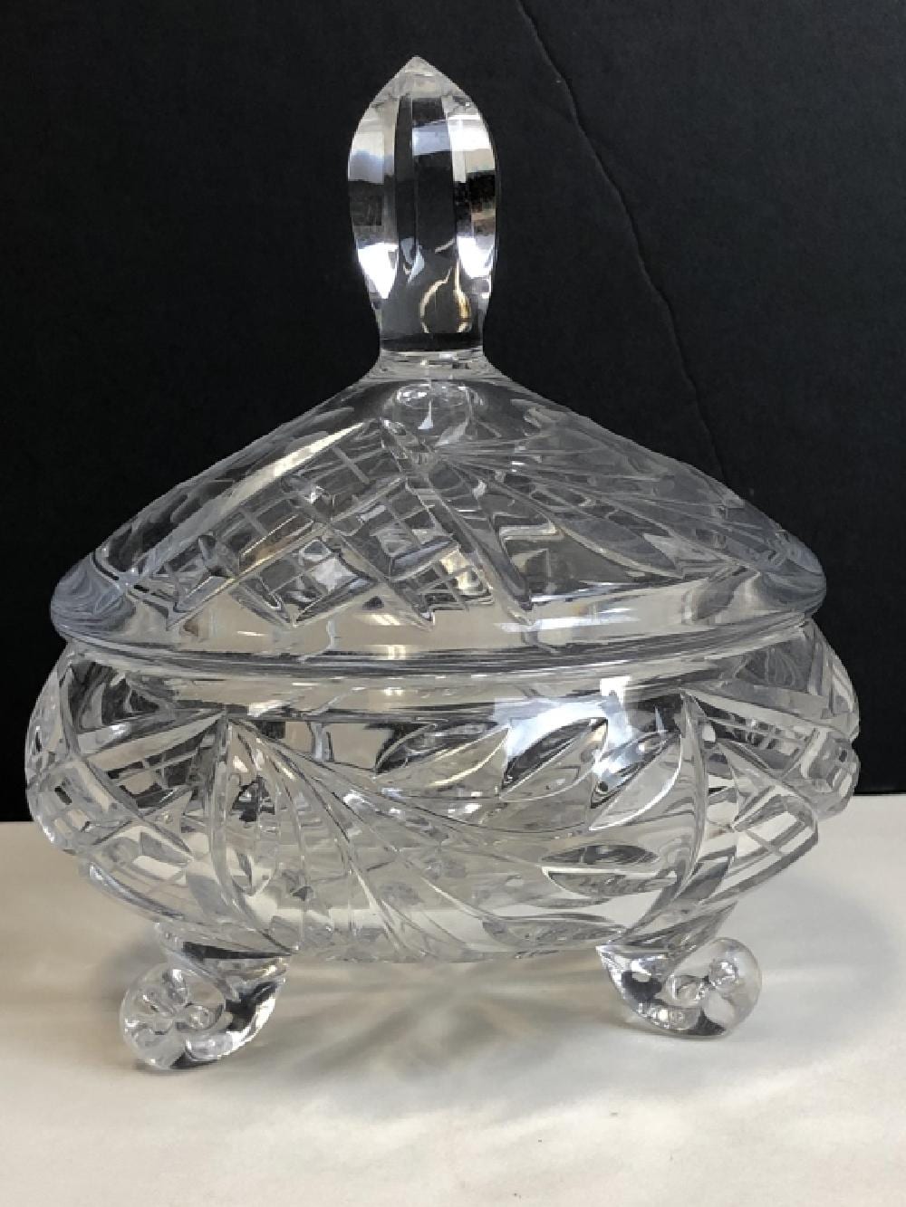 Clear glass compote with faceted sides and a scalloped rim on three short footed legs.