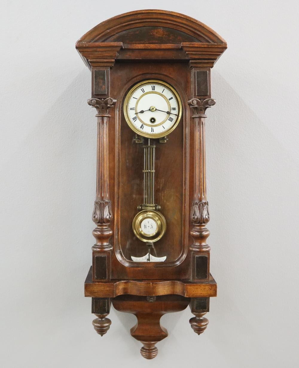 Wall clock with arched wooden case, round white clock face with gold ring, and small dial below.