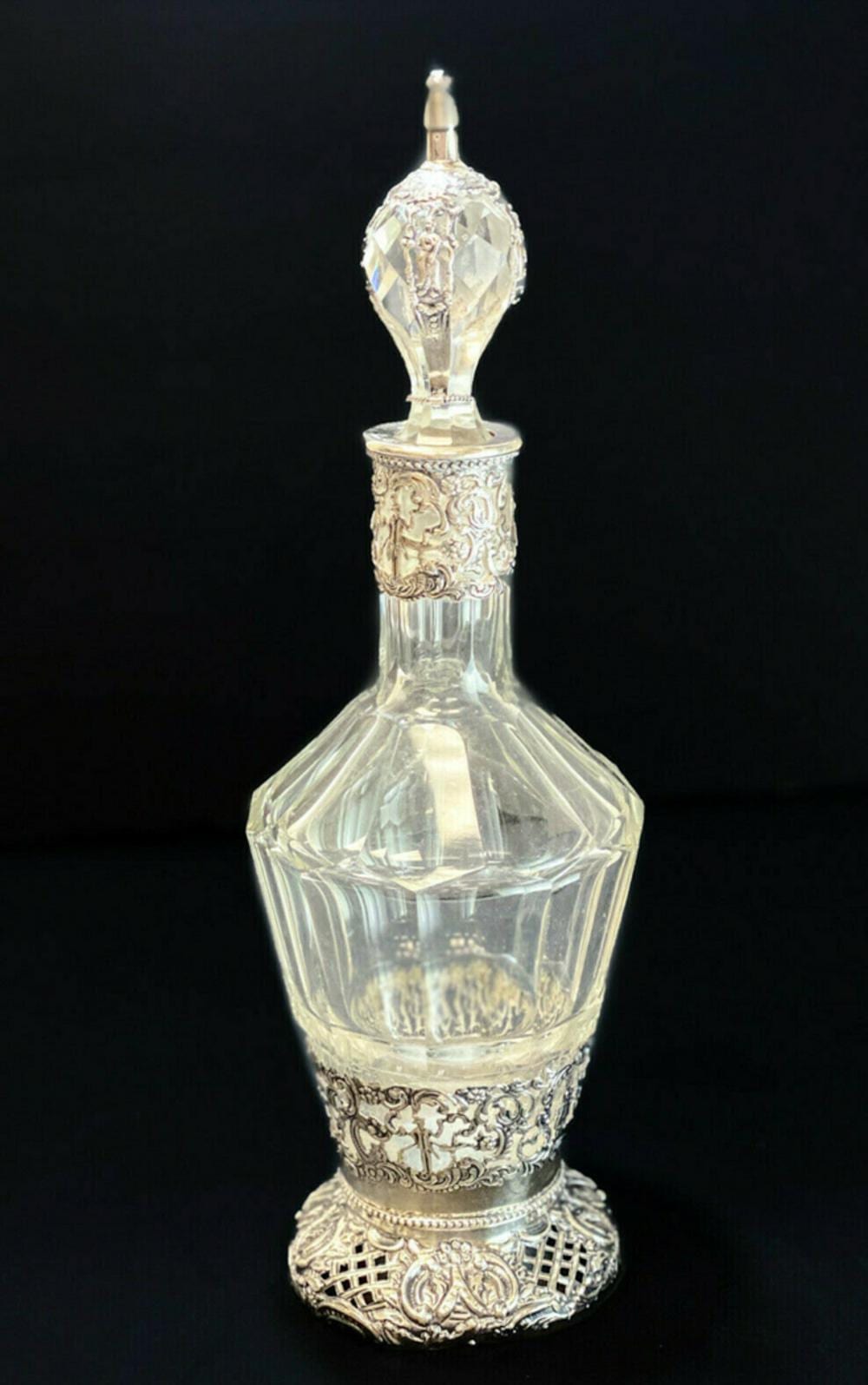 Tall cut-glass decanter with diamond-pattern stopper and silver-colored ornate collar and base on a dark background.