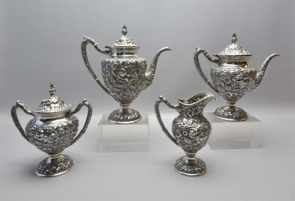 Four pieces of silver-tone tea set—two teapots and two matching condiment/creamers—each with embossed floral designs and ornate lids and handles.