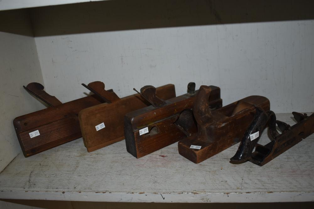 Five brown vintage wood hand planes arranged on a white workbench against a wall.