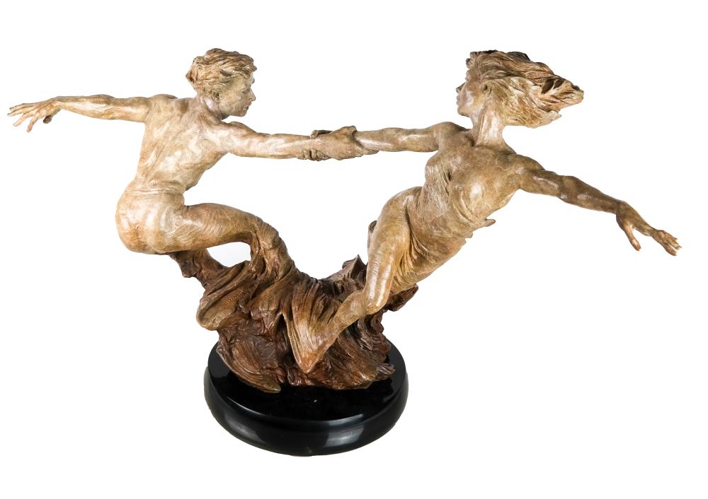 Two bronze figures in a dynamic dance pose, balanced on a dark circular base against a white background.