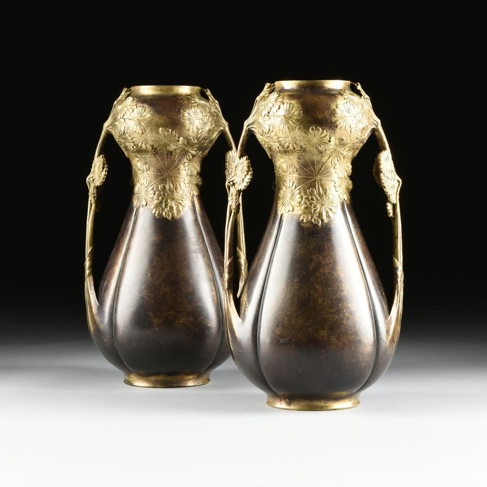 Pair of ornate metal vases with gold rims and floral relief decoration, shown side by side against a dark background.