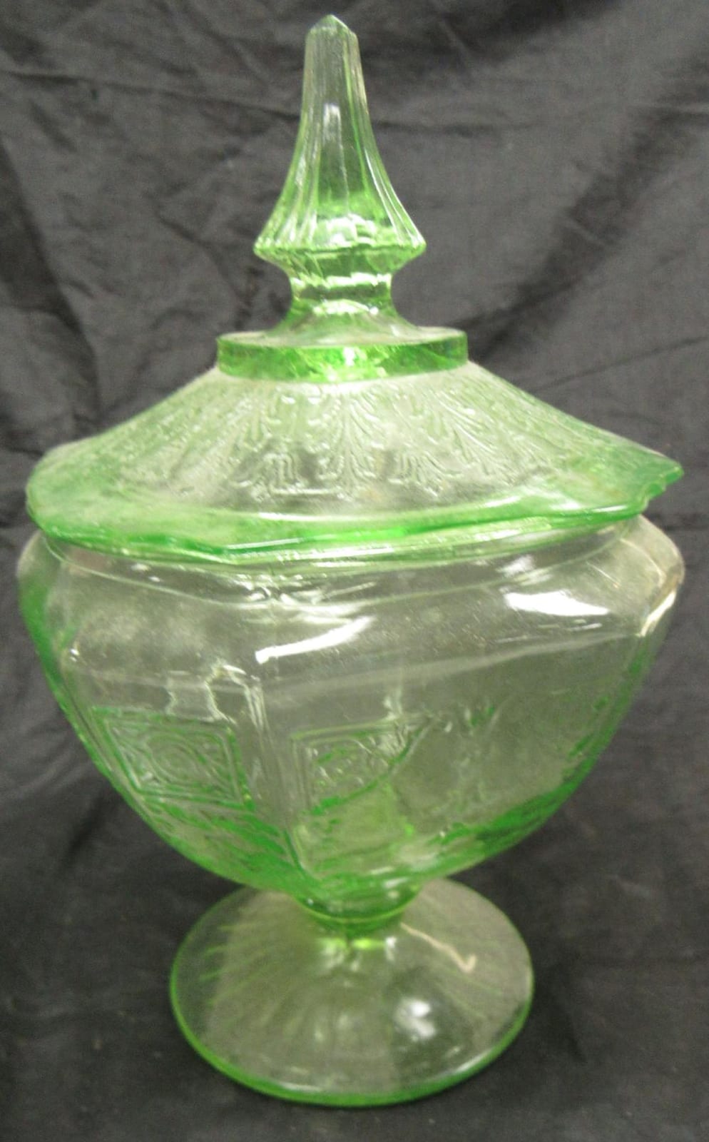 Green footed glass candy dish with lid, shown on a pedestal base against a dark background.