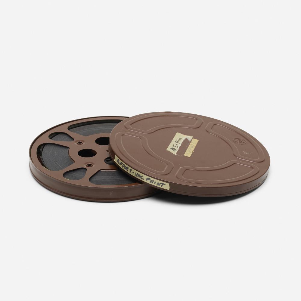 Brown plastic film reel with a small label visible on the top cover; the film strip shows dark holes around the edge.