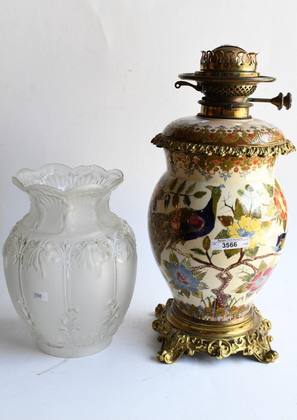 Two decorative oil lamps on a white background: a glass lamp with embossed floral scene and a brass-mounted painted ceramic banquet lamp with a crown-like top.