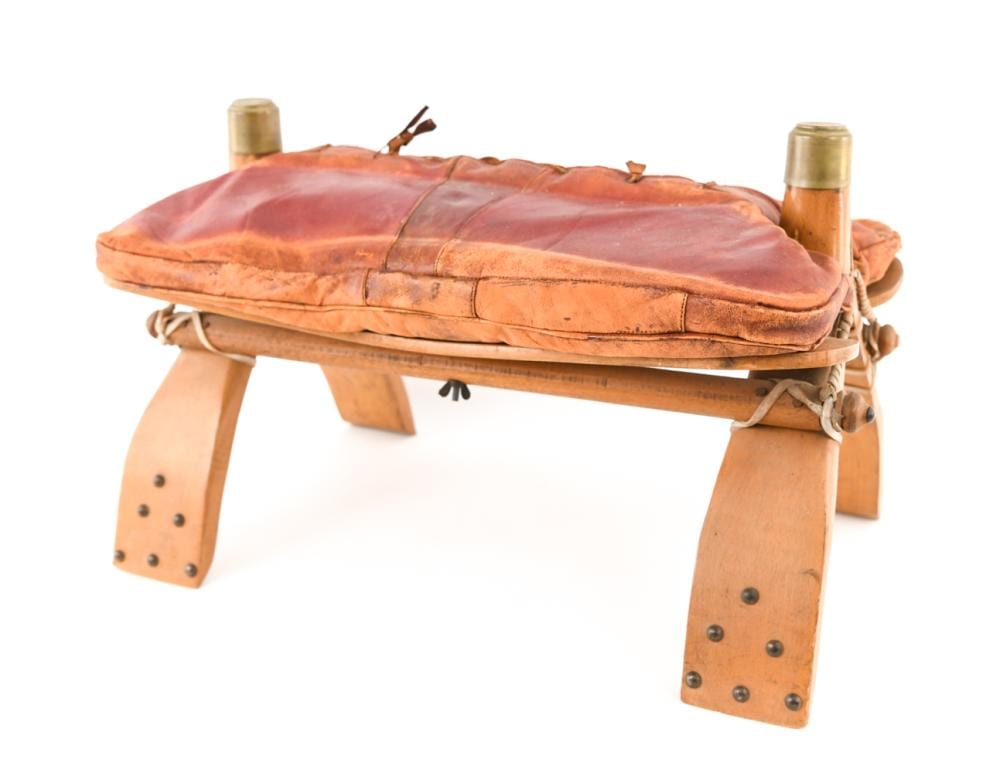 Vintage camel saddle-style ottoman with brown leather seat cushion on a wooden frame, shown on white background.