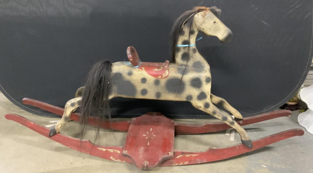 Painted wooden rocking horse with dark mane and spotted light-and-dark body, on a red and white rocking base.