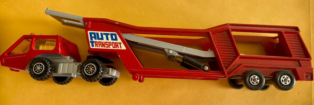 Red toy car transporter truck with a crane arm and a small gray-and-red car on a yellow background.