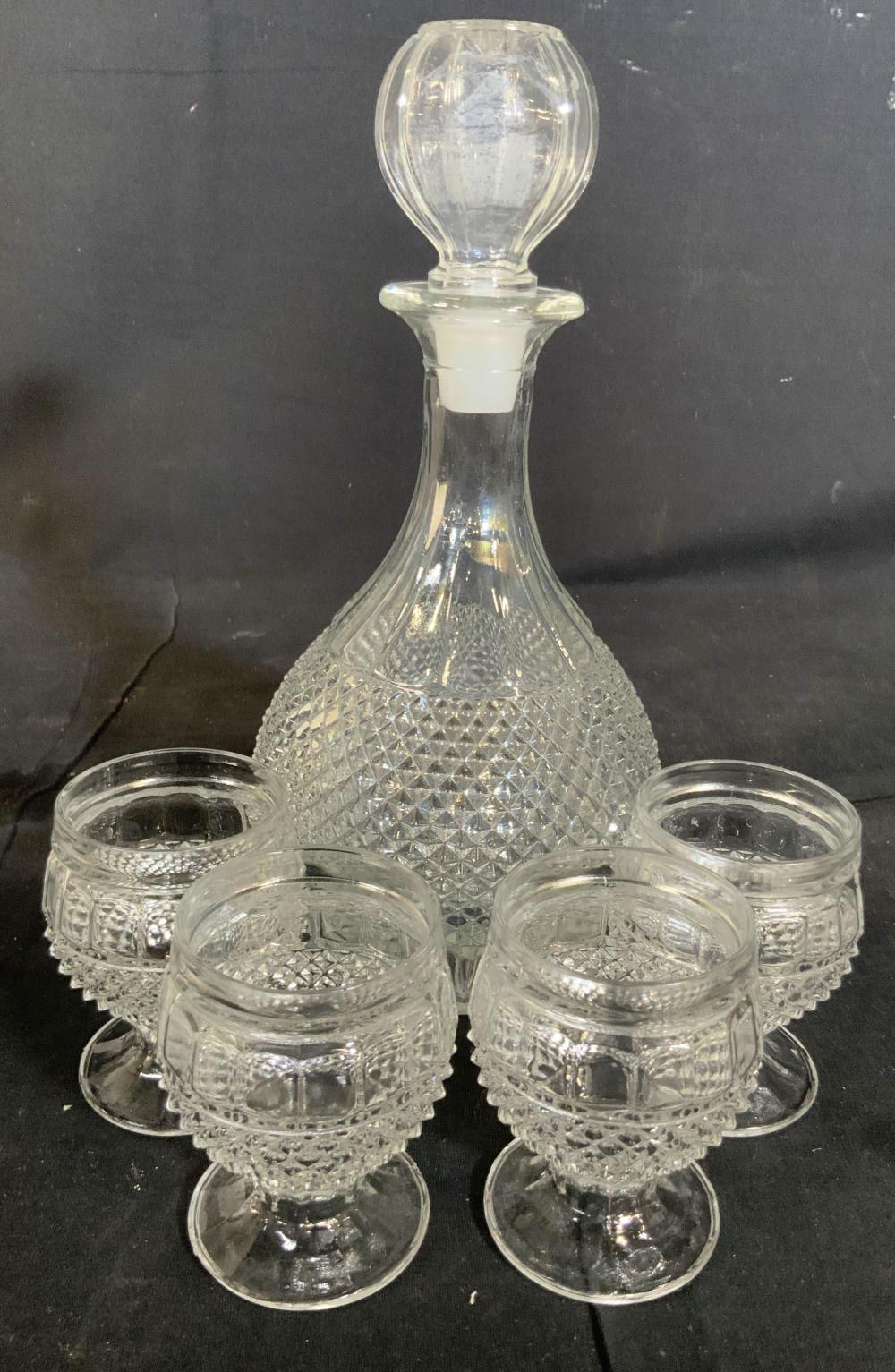 Clear cut-glass decanter with a stopper and four matching small glasses on a dark background.