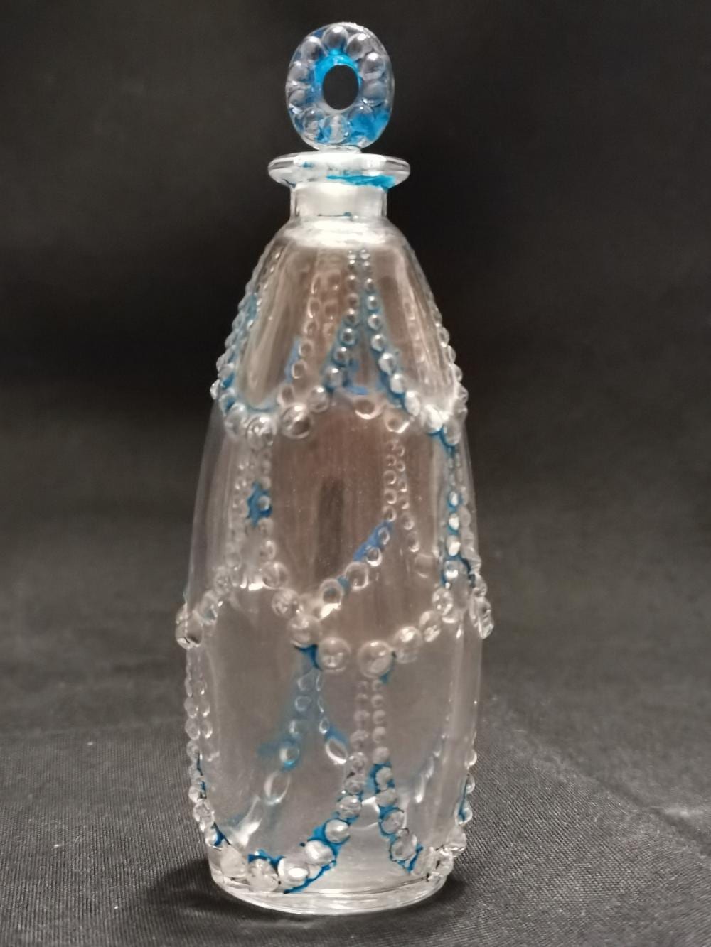 Clear glass perfume bottle with blue decorative accents and a faceted oval stopper.