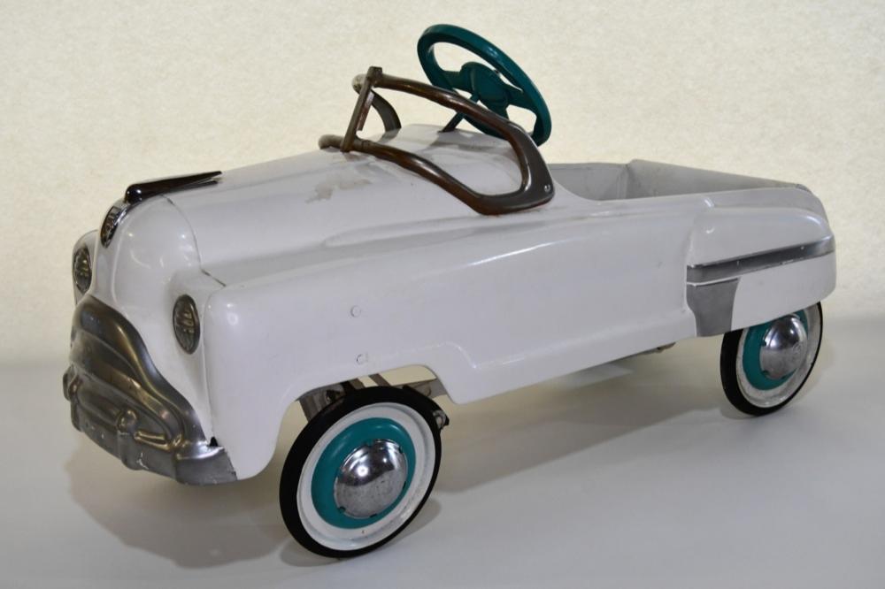 White toy pedal car with teal wheels and a brown steering handle on a light background.