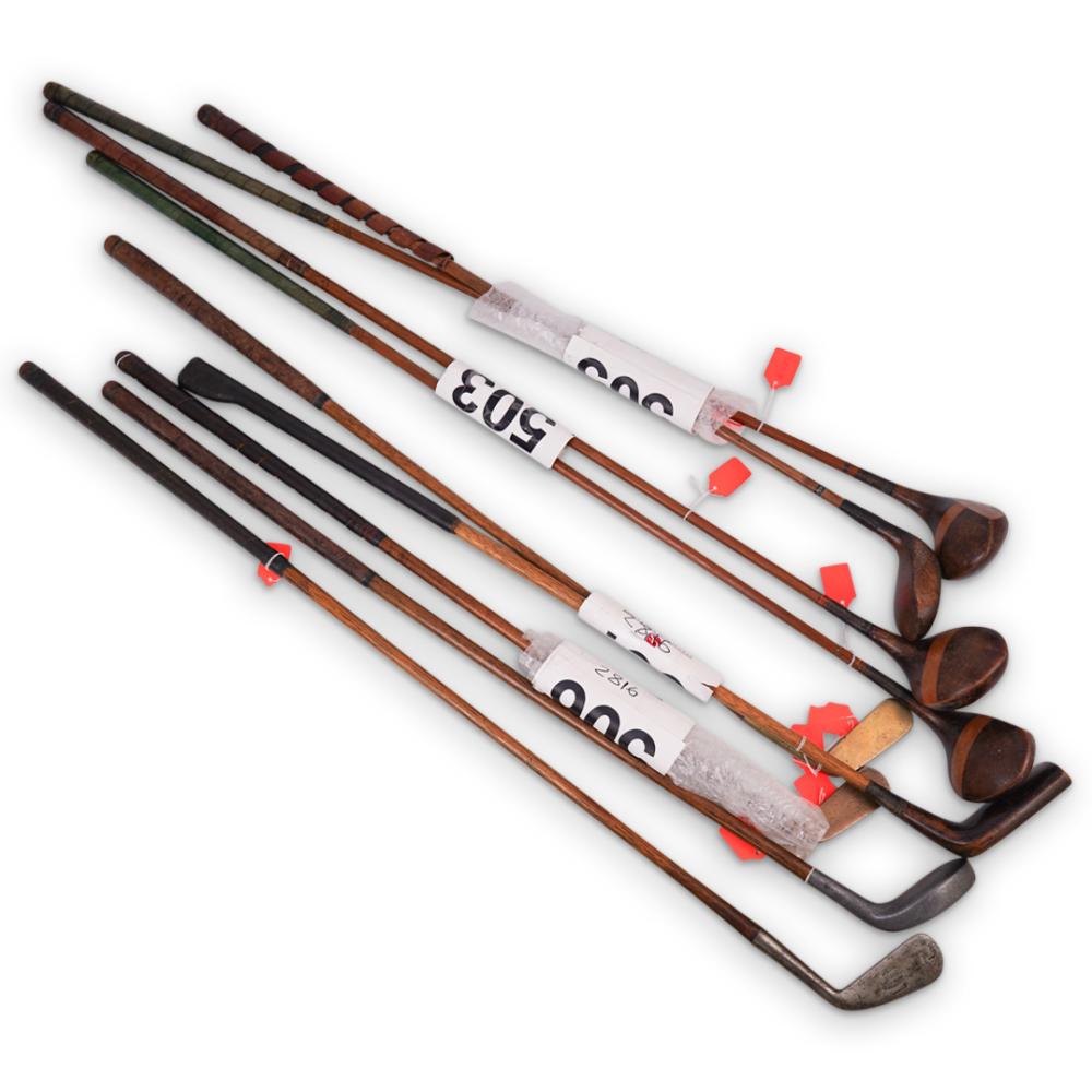 Nine vintage golf club shafts and wooden club heads laid out on a white background, with red tags on the grips.