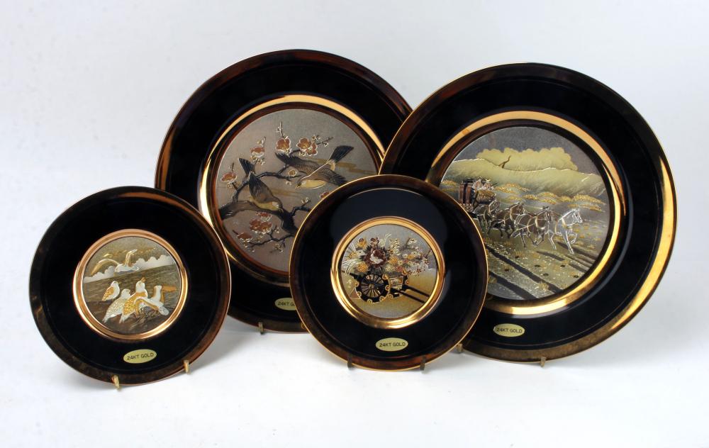 Set of four round decorative plates with dark rims and gold-bordered scenes, including birds on branches, a horse carriage, and a landscape with people.