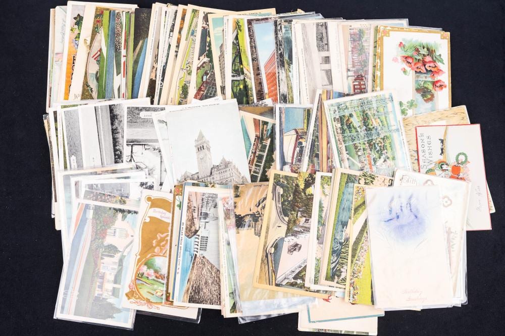 Assorted vintage postcards fanned and stacked together on a dark background, showing colorful city and scenic scenes.