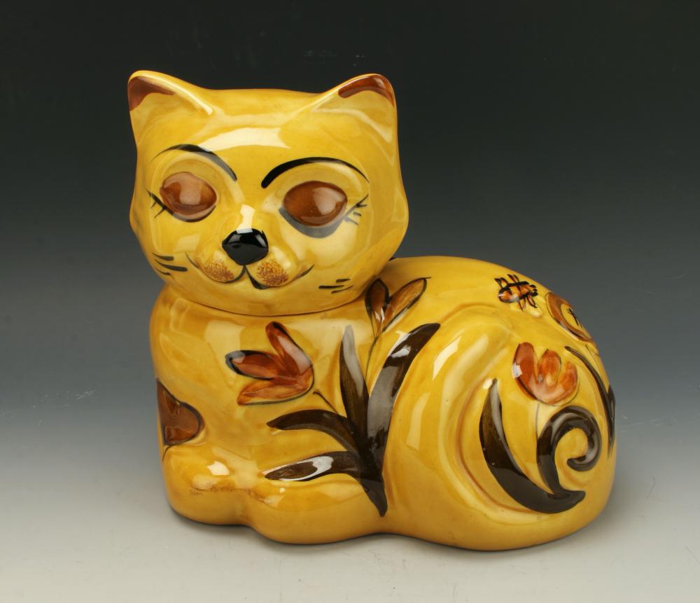 Yellow cat-shaped cookie jar with painted face, curled body, and molded paw and tail details on a light background.