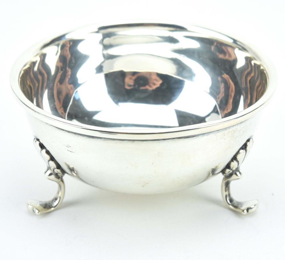 Shallow round silver-colored footed salt cellar with three paw-shaped feet and a polished reflective interior.