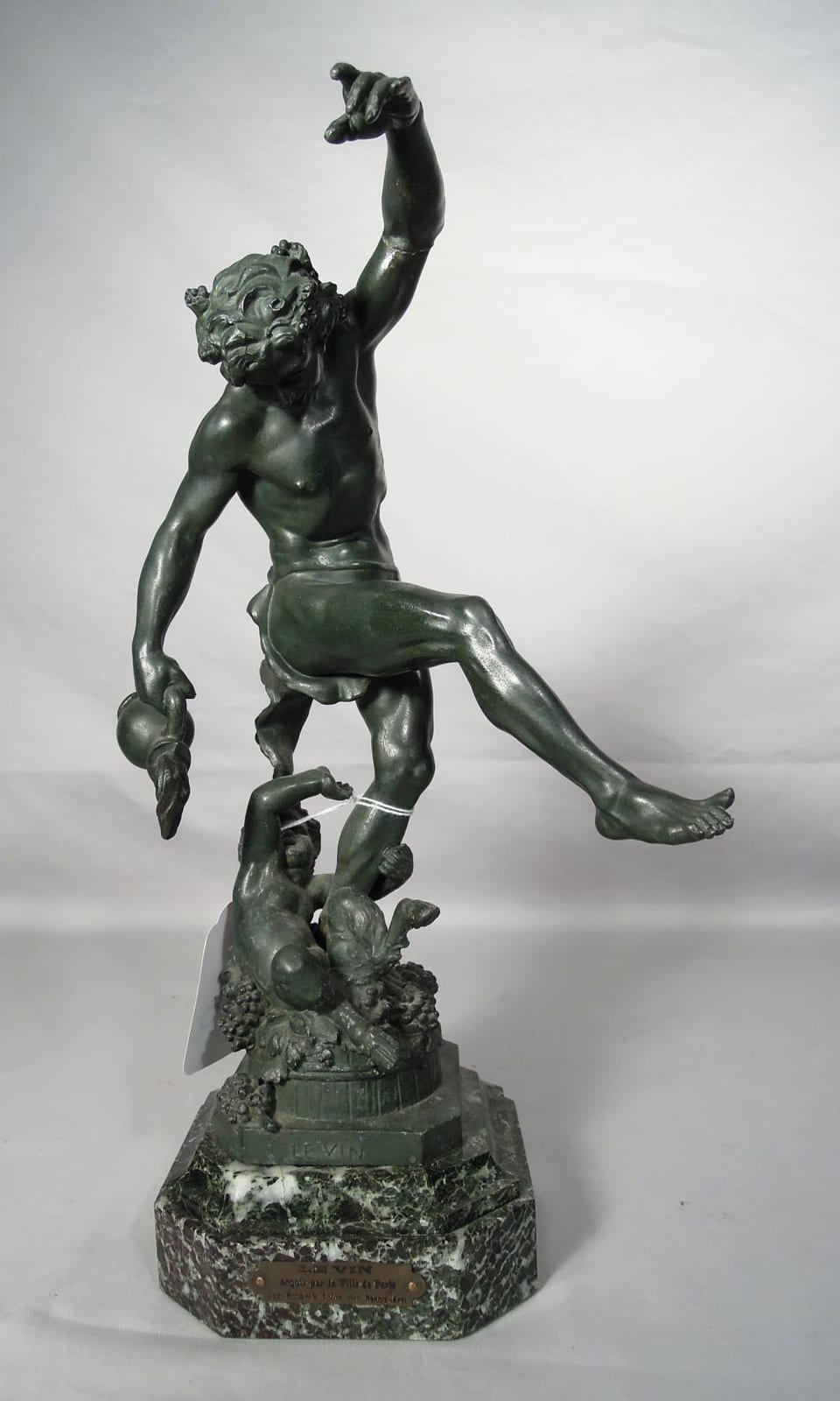 Green bronze-toned sculpture of a dancing nude woman with one arm raised, standing on a base with an additional small figure near her feet.