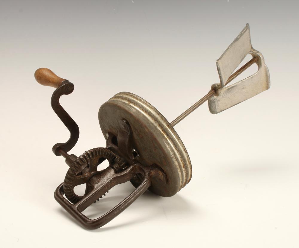 Hand crank butter churn mechanism with a large metal churn disk, metal arms, and a wooden handle on a light background.