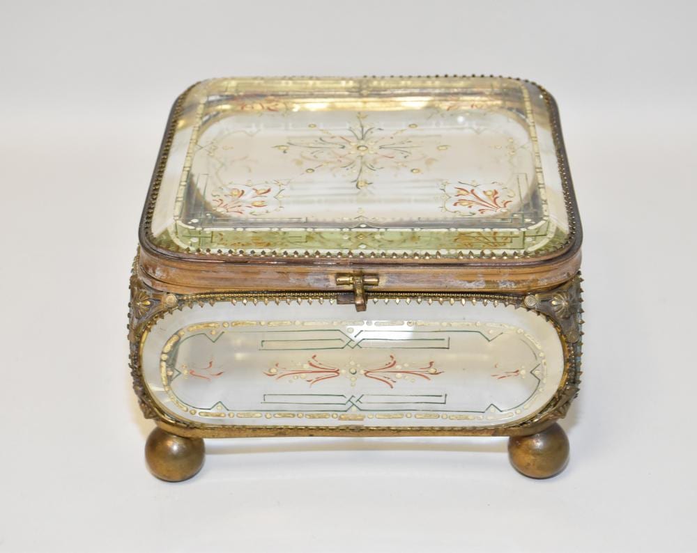 Open ornate jewelry casket with glass top lid, gold-tone metal frame, and decorative floral pattern on the interior.