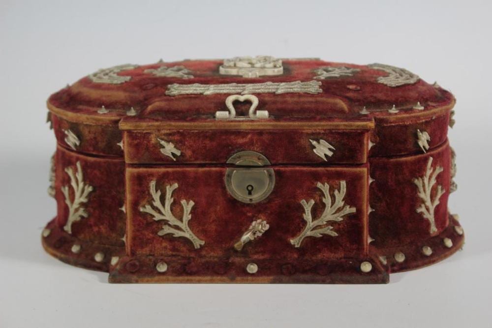 Closed maroon velvet sewing box with brass lock on the front and decorative white metal leaf accents around the sides and lid.