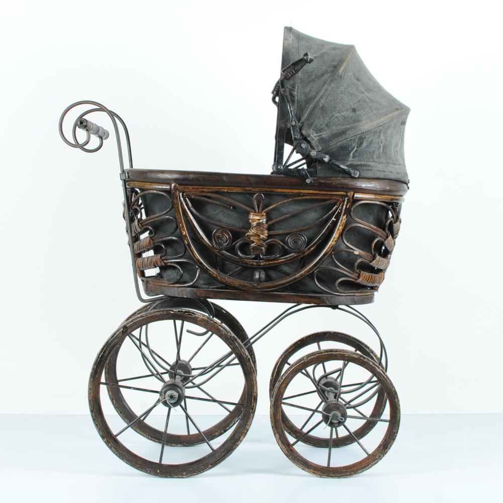 Vintage doll carriage stroller on four spoked wheels with a dark fabric canopy and decorative metal frame.