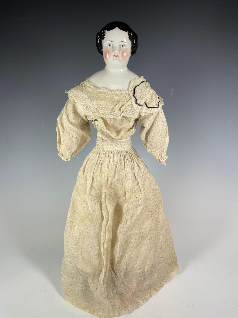 Porcelain doll figure with pale face, red lips, black molded hair, and a cream lace-style dress with long sleeves.