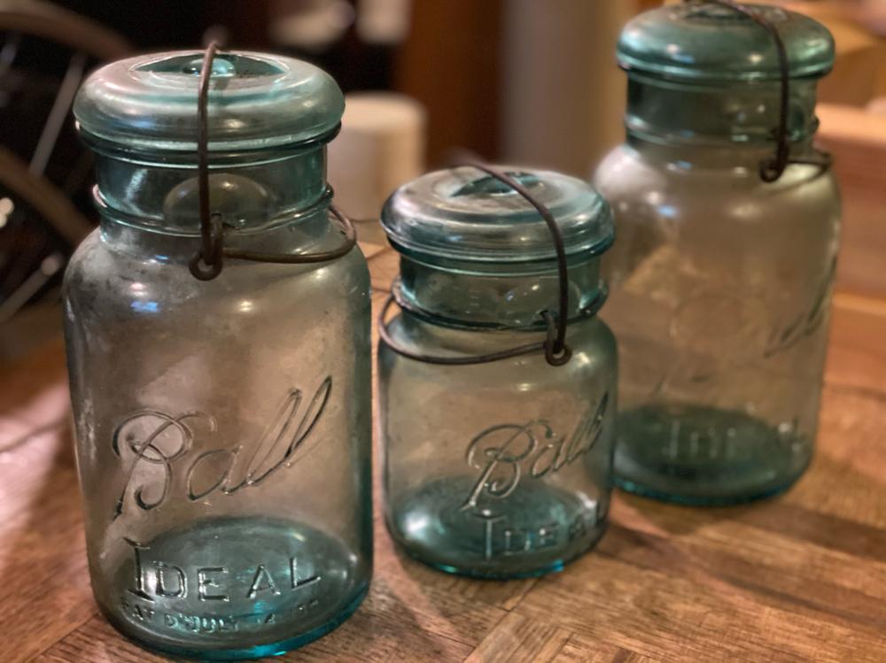Three clear glass mason jars with blue-green lids and hanging wire closures on a wooden surface.