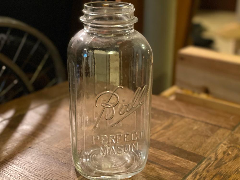Glass mason jar with embossed lettering on a wooden table, shown close-up with threaded top.